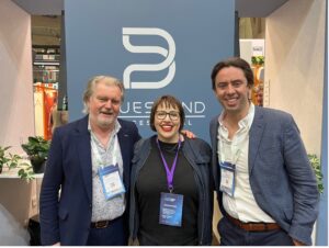 Two gentlemen and one lady standing in front of Bluesound Professional banner